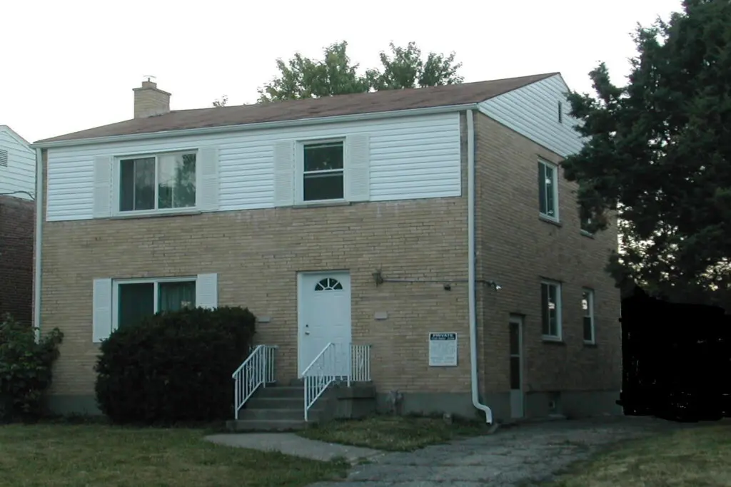 A two-story brick house with a white door and siding on the upper level.
