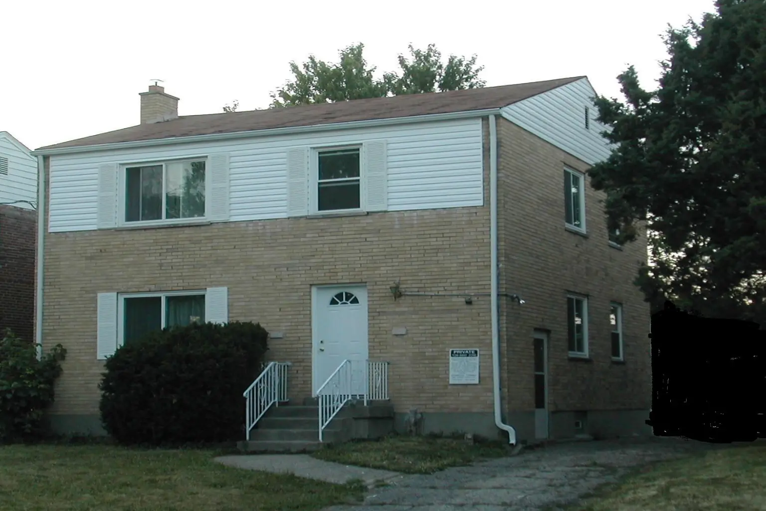 A two-story brick house with a white door and siding on the upper level.